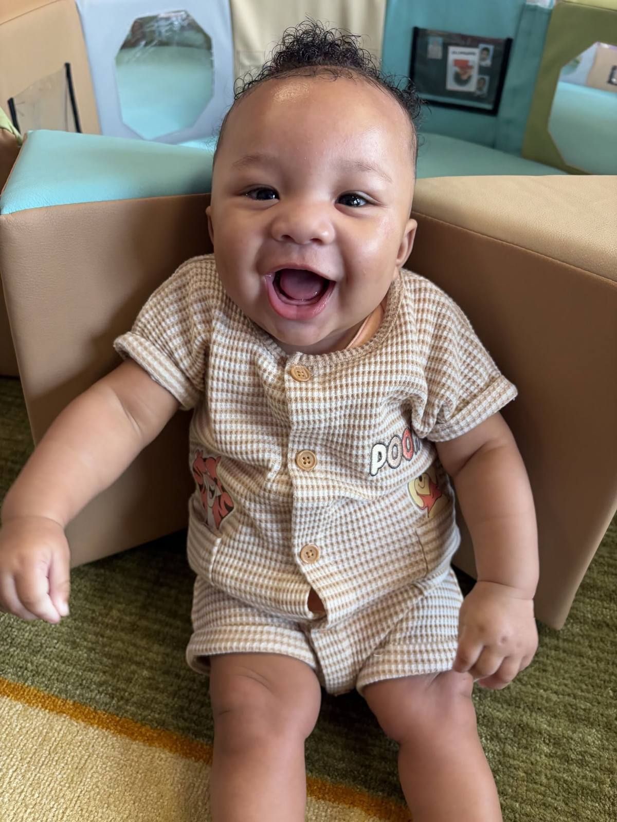 A smiling baby sitting up in a cozy corner of the infant room