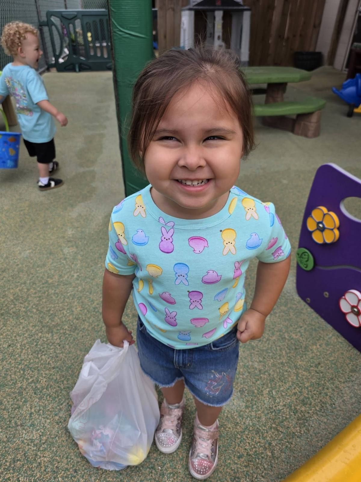 A grinning preschooler with a bag of treats on the playground