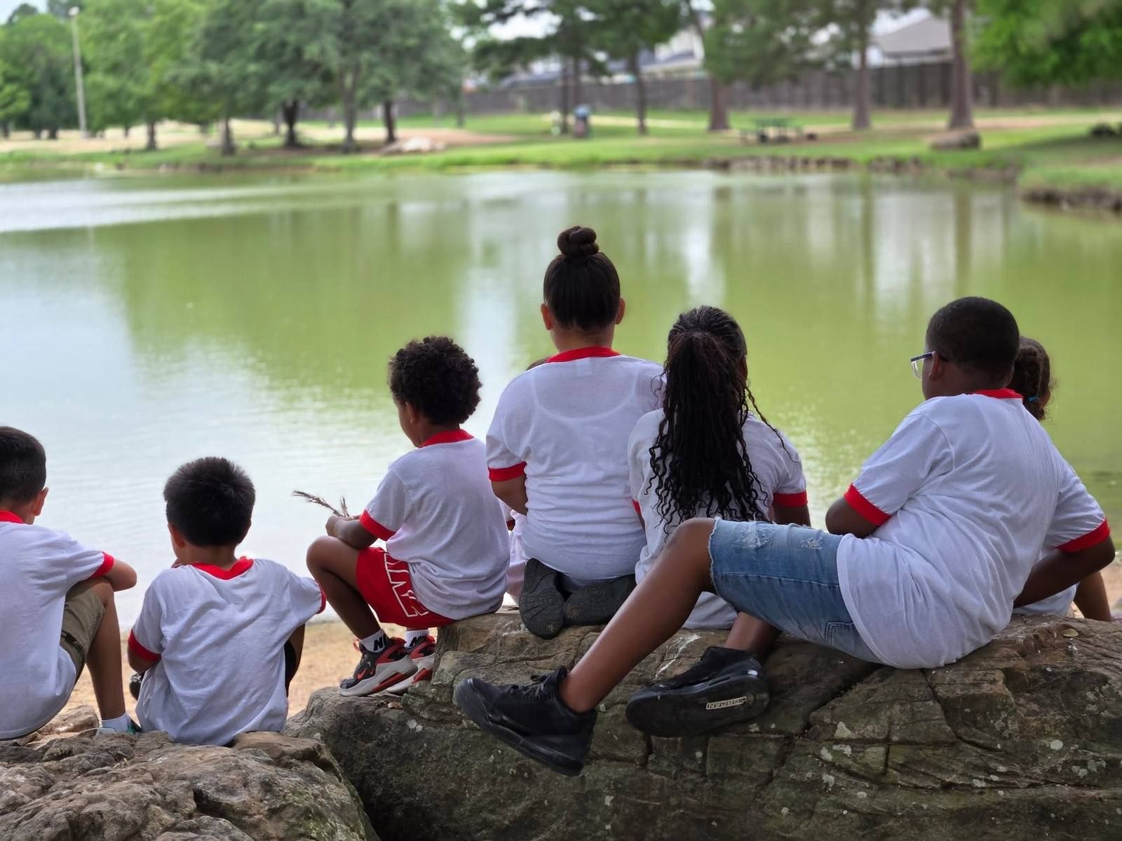 School age kids sitting on a rock looking out over a pond on a field trip
