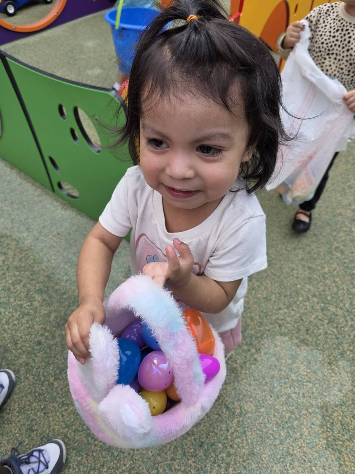 A smiling toddler holding a basket of eggs at the Kidco egg hunt