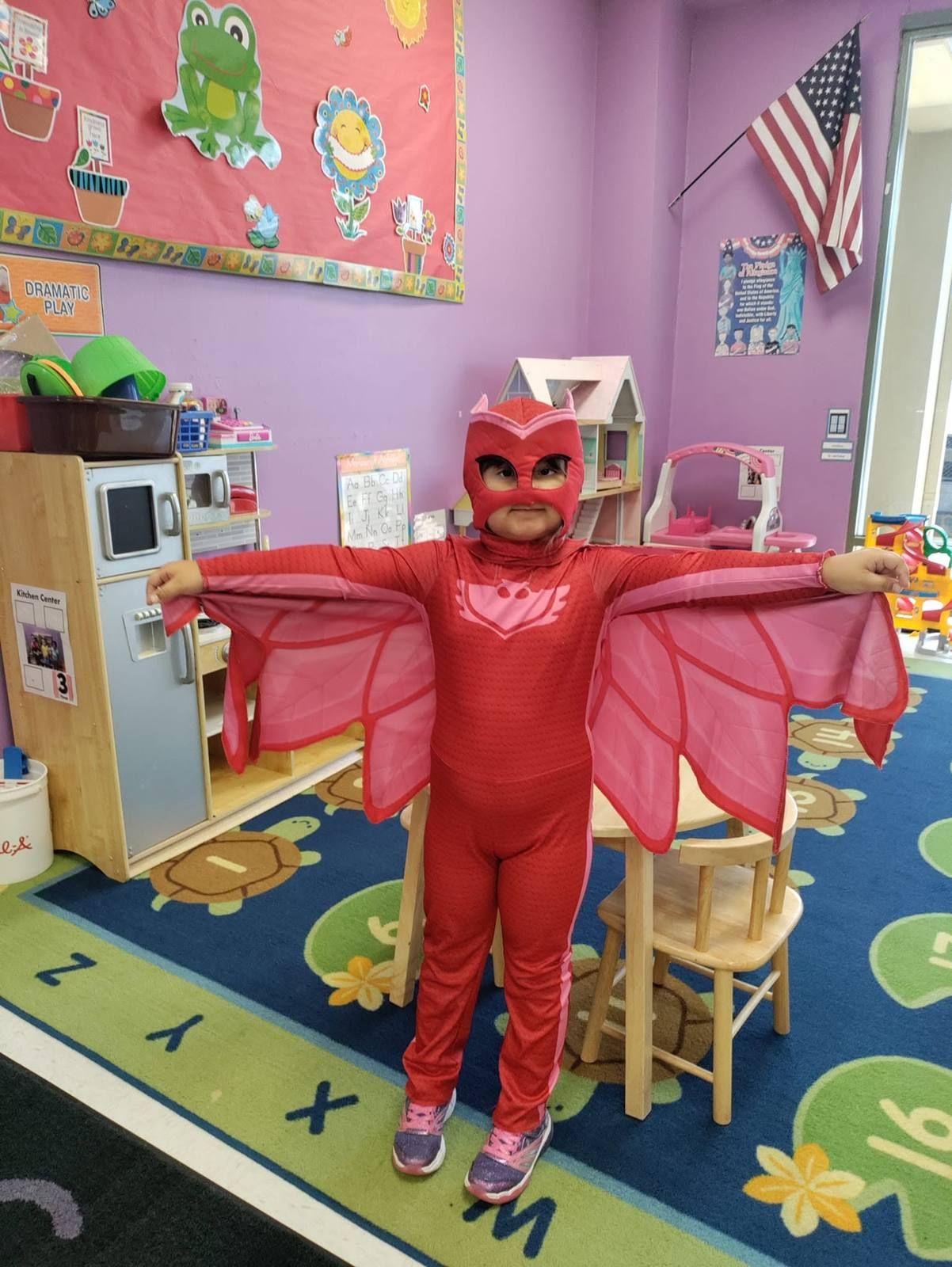 A preschooler in a red superhero costume spreading her wings