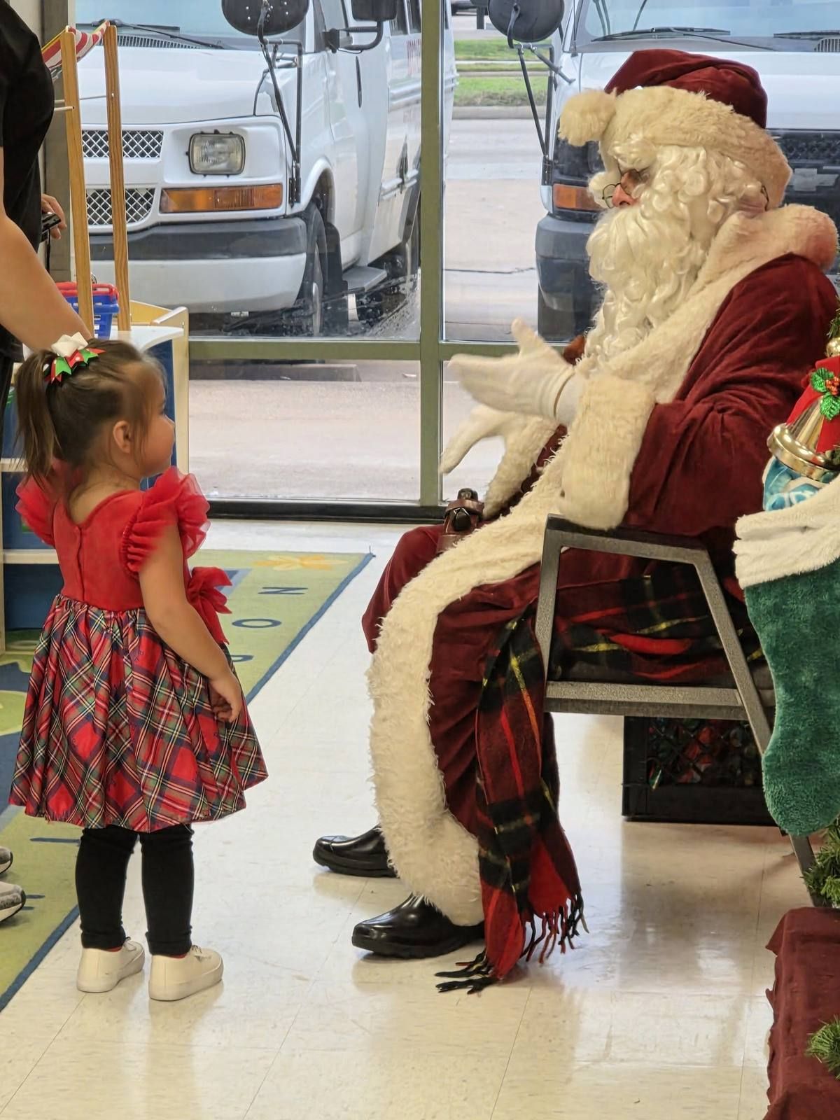 A toddler in a holiday dress meeting Santa in the lobby