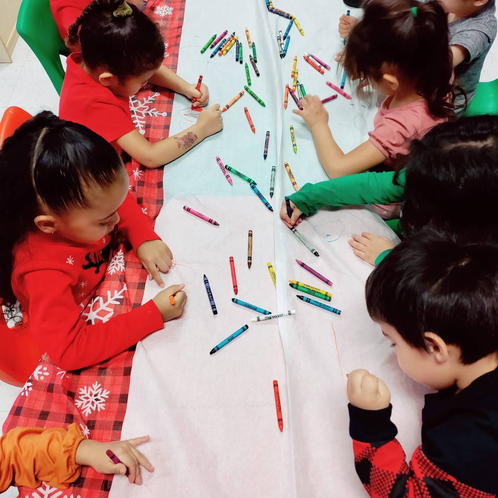 Kids coloring together on a long paper-covered table