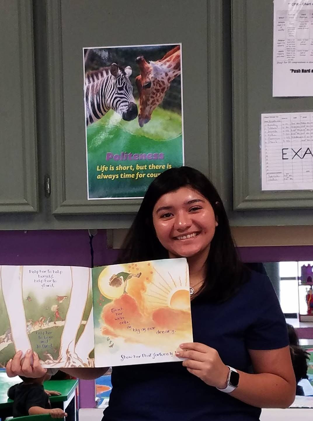 A smiling teacher holding up a picture book during story time