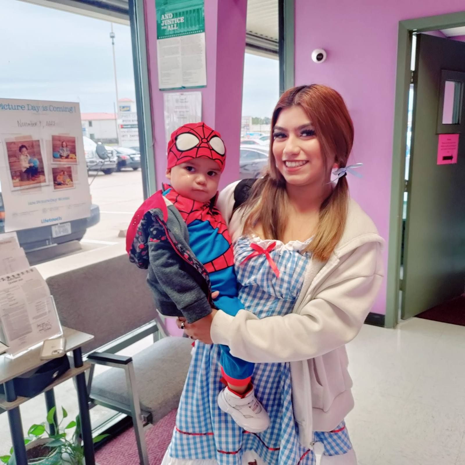 A teacher in a Dorothy costume holding a baby dressed as a superhero