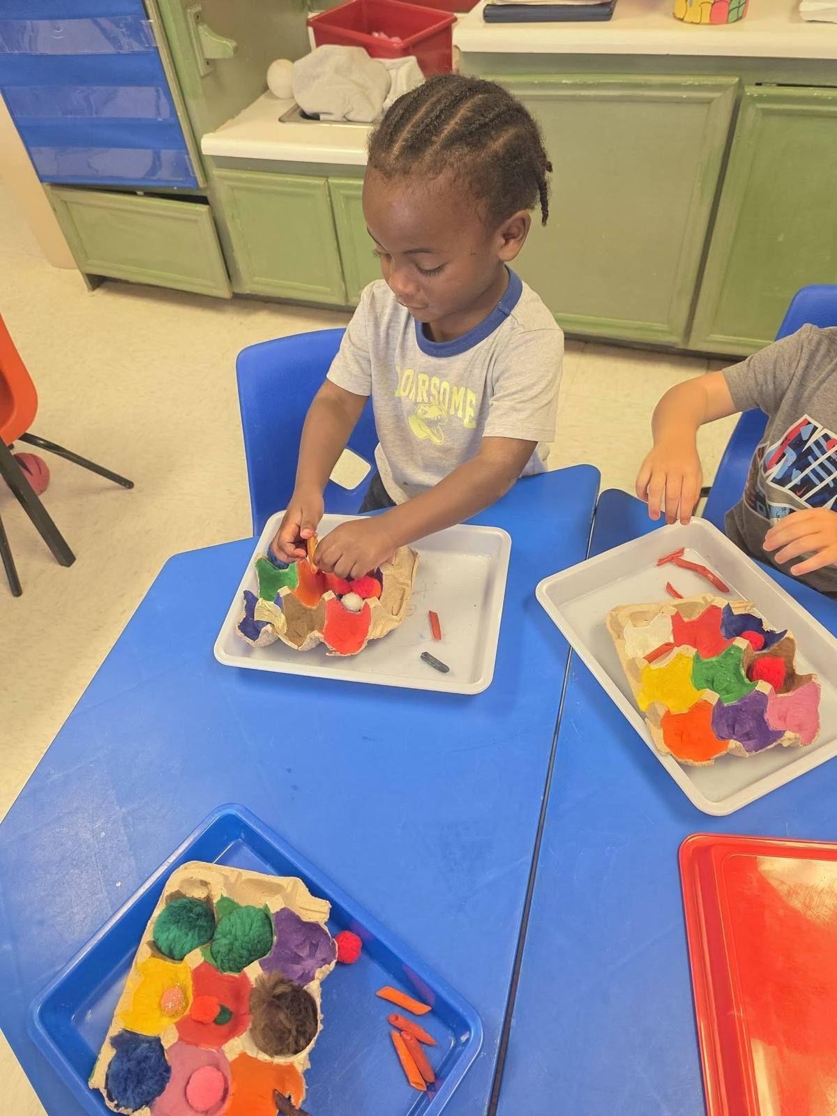 A boy sorting colored pom-poms into an egg carton at Kidco