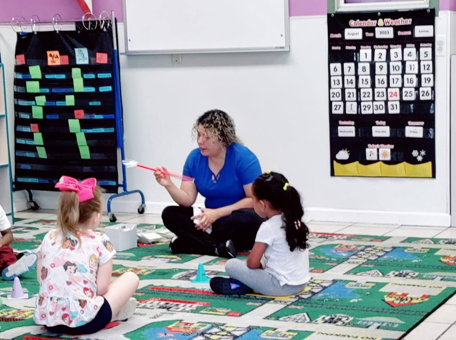 A teacher and preschoolers playing a game on the rug
