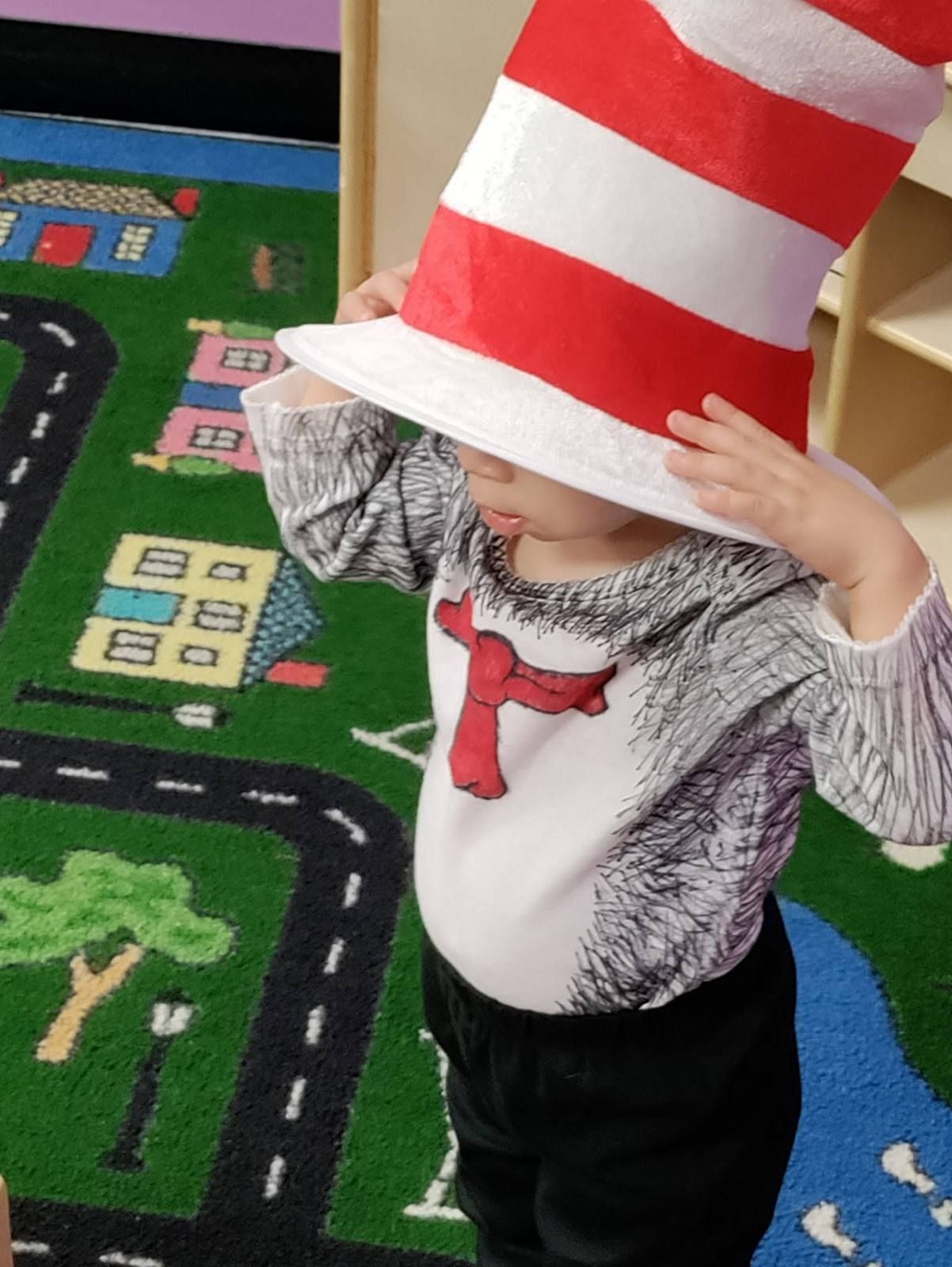 A toddler trying on a tall striped hat