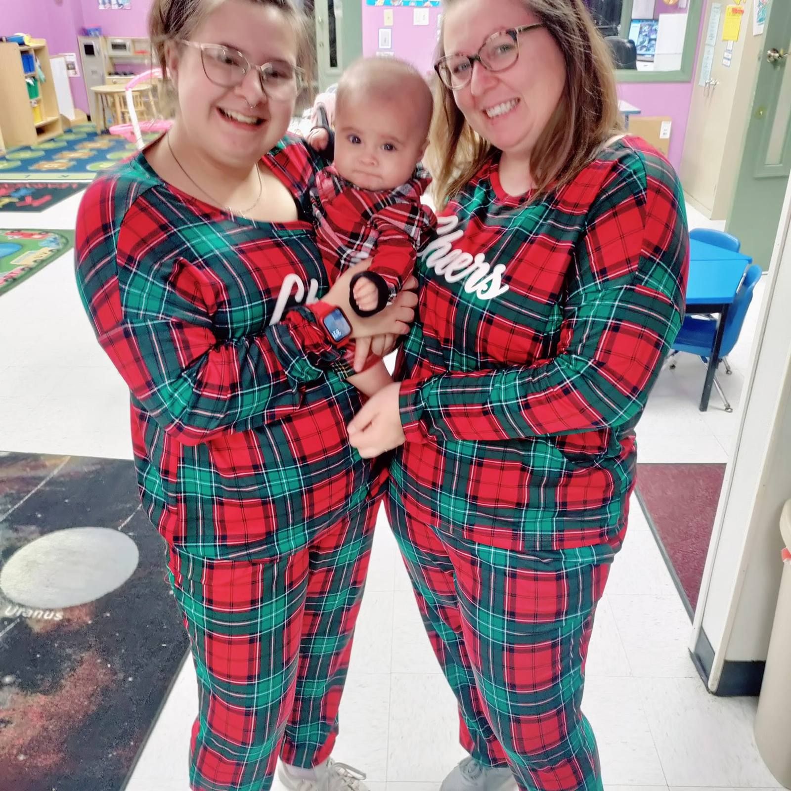 Two teachers in matching pajamas holding a baby