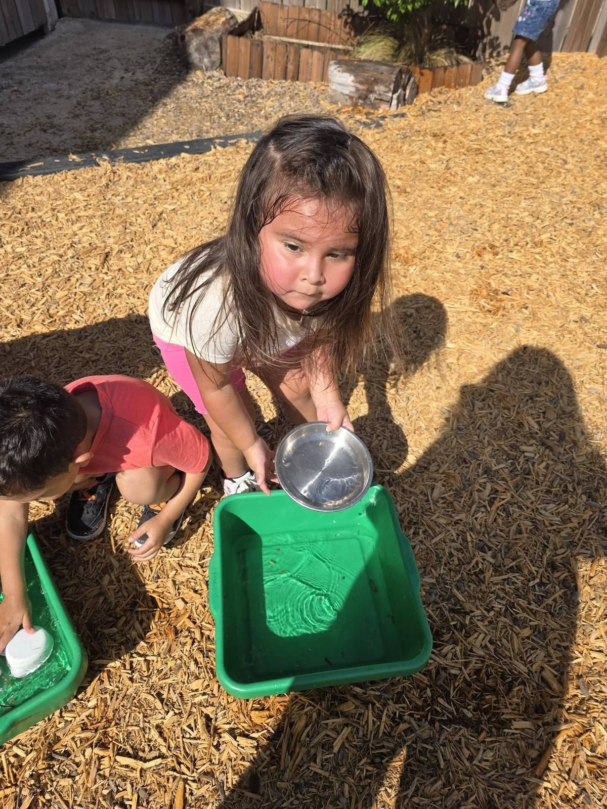 A preschooler playing with bowls and water in the wood chips