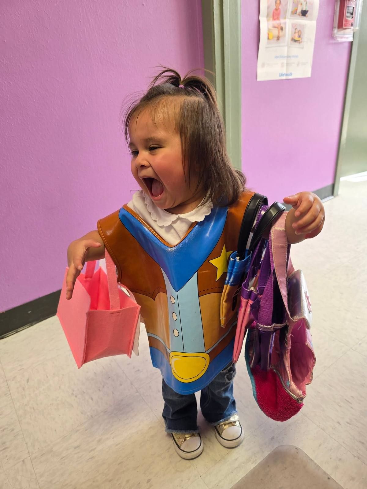 A toddler in a cowboy vest shouting with joy while carrying bags