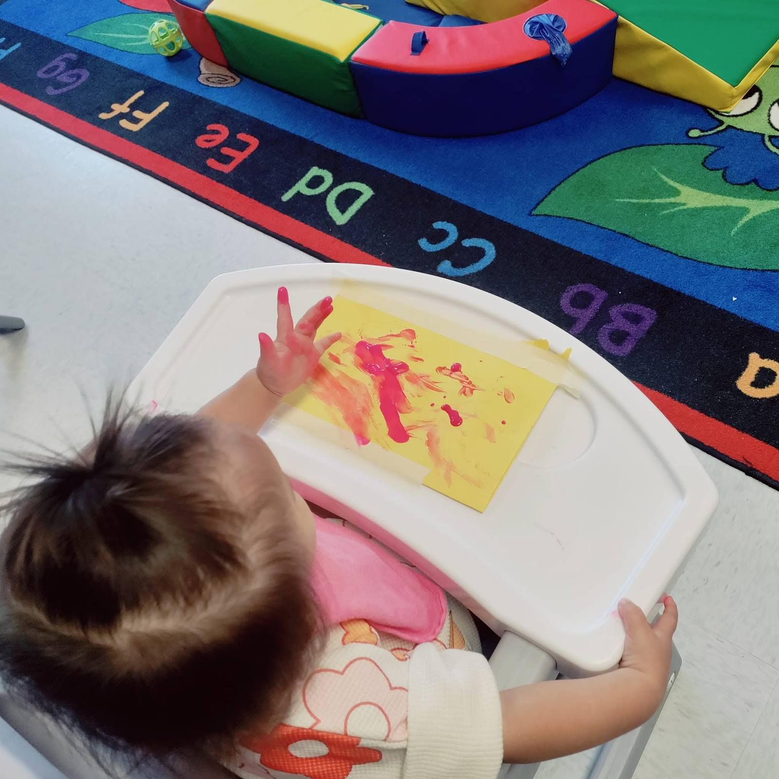 A baby finger painting in a high chair
