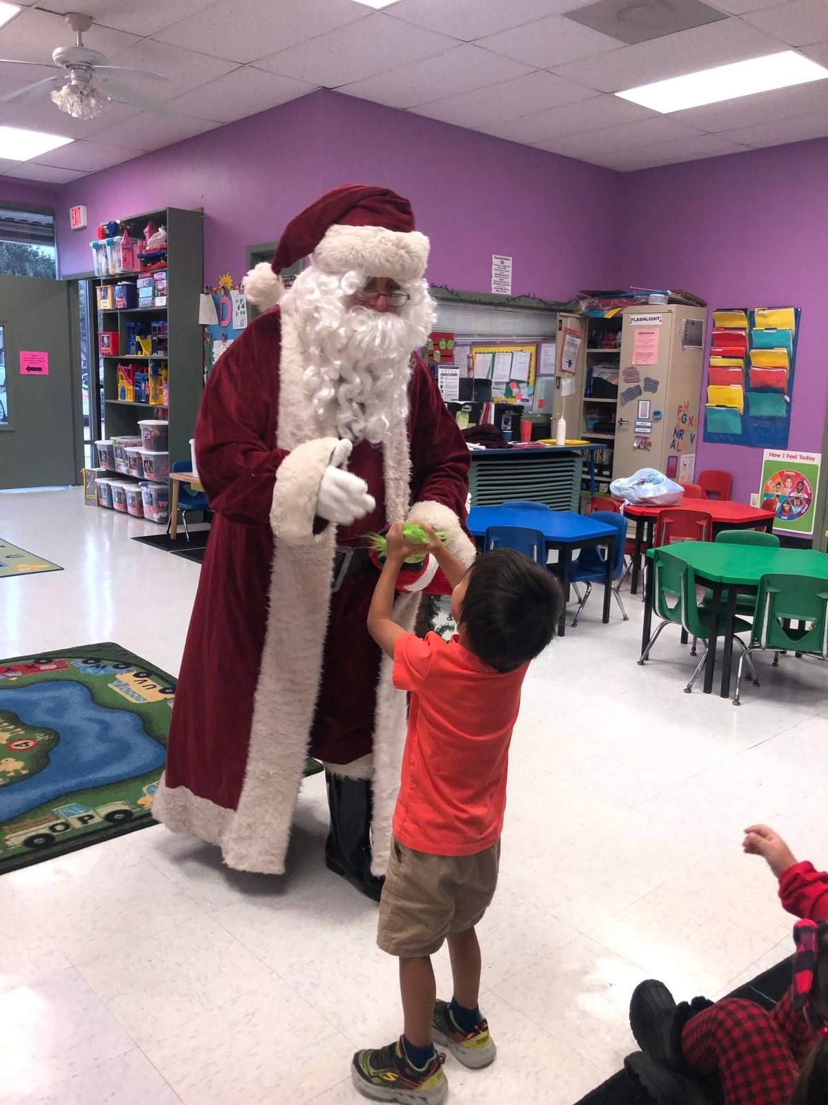 Santa handing a small gift to a boy in the classroom