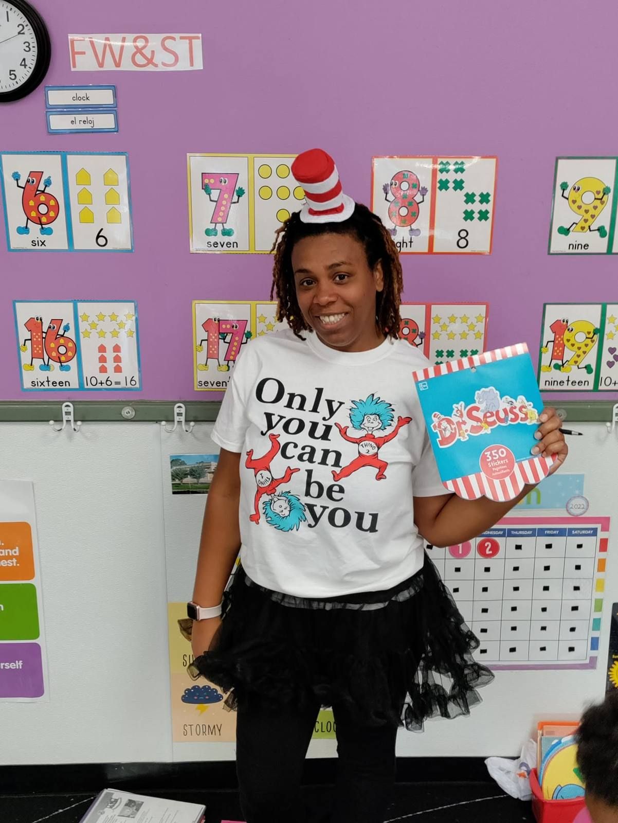 A teacher in a striped hat holding a Dr. Seuss book