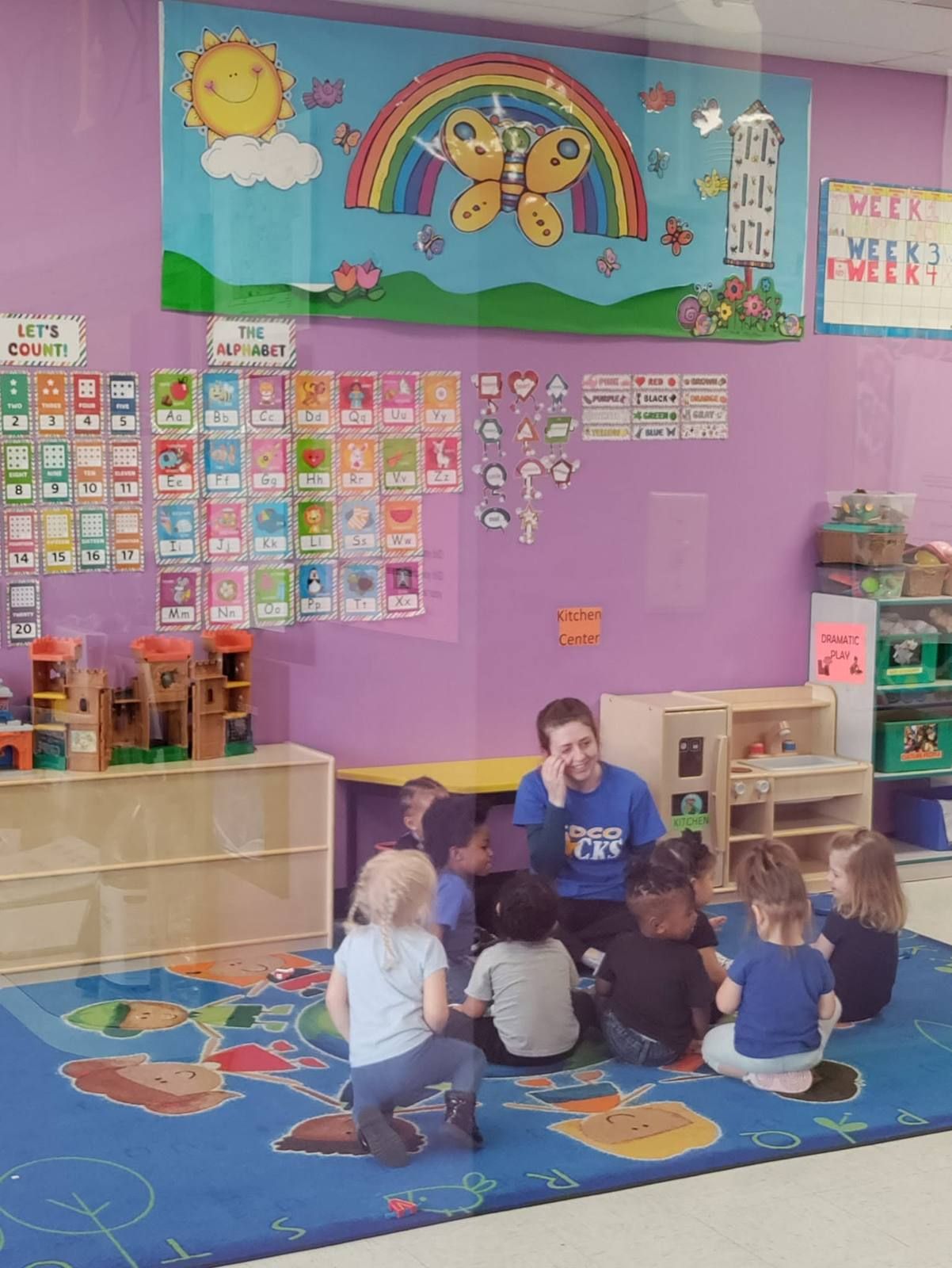 A toddler class gathered on the rug with their teacher