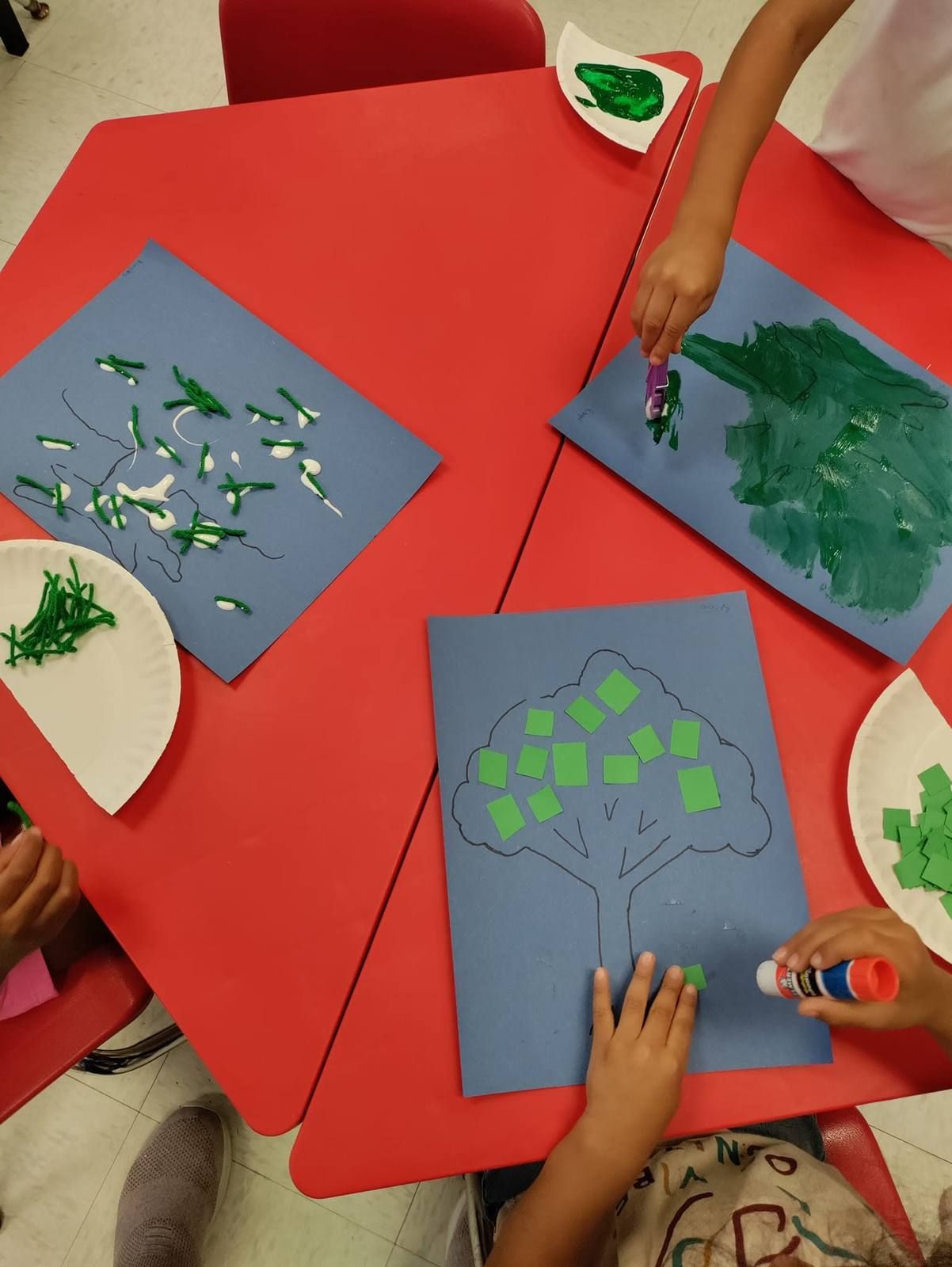 Kids gluing paper leaves onto tree pictures