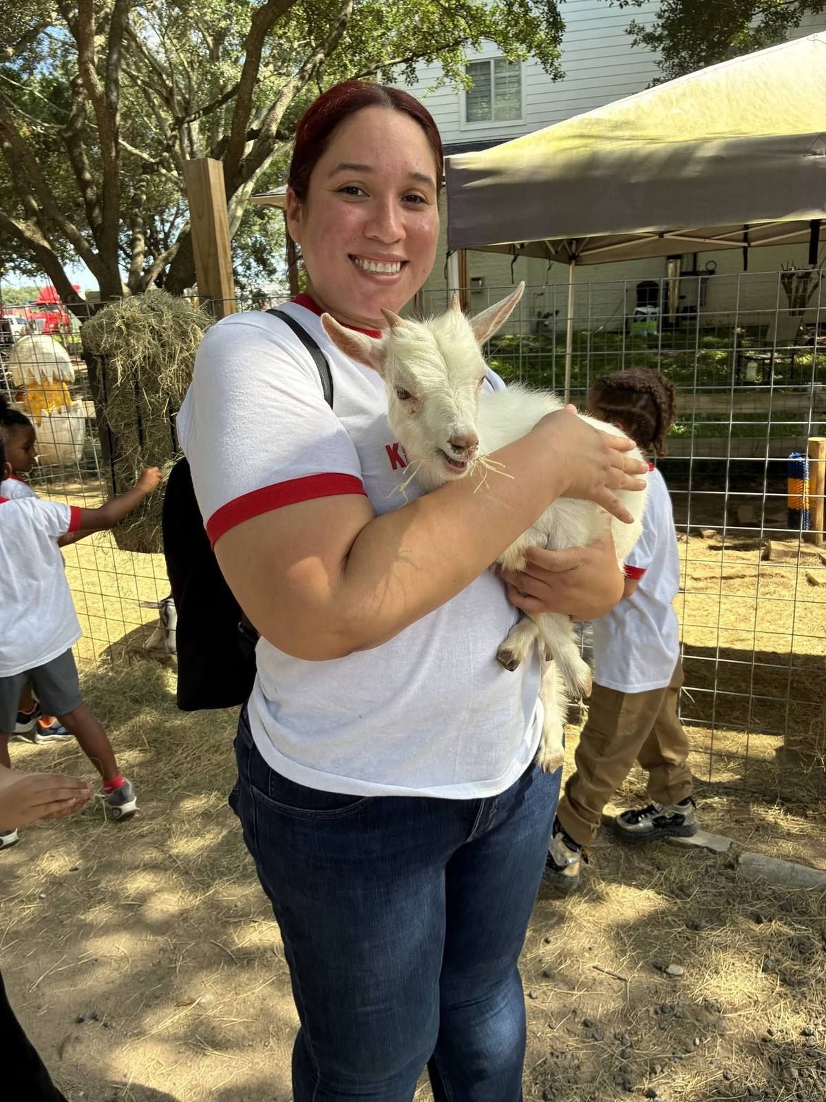 A smiling teacher holding a baby goat at the farm