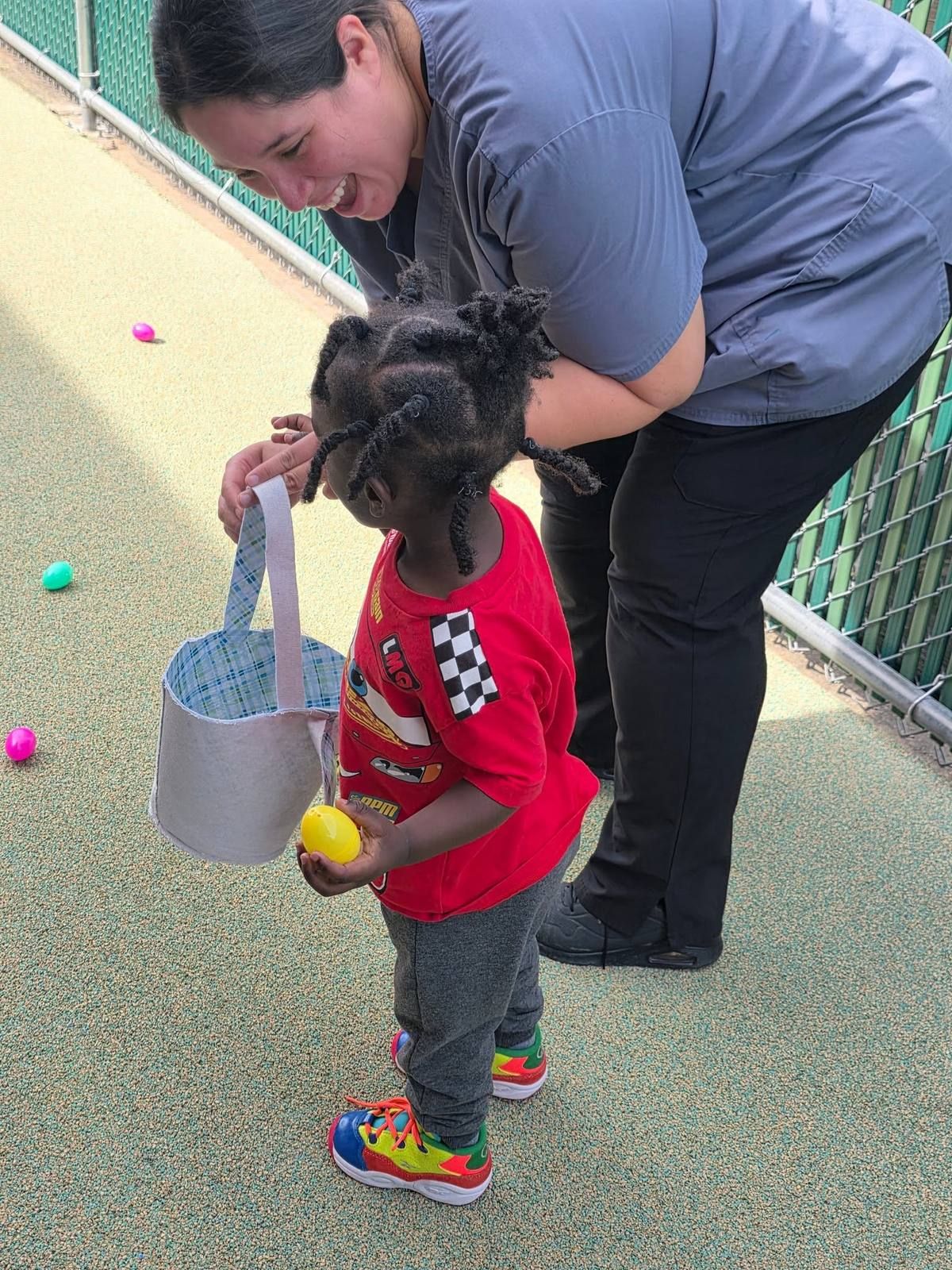 A teacher helping a toddler with an egg basket