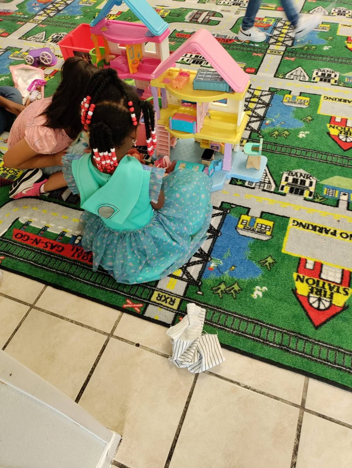Two girls playing with a dollhouse on the rug