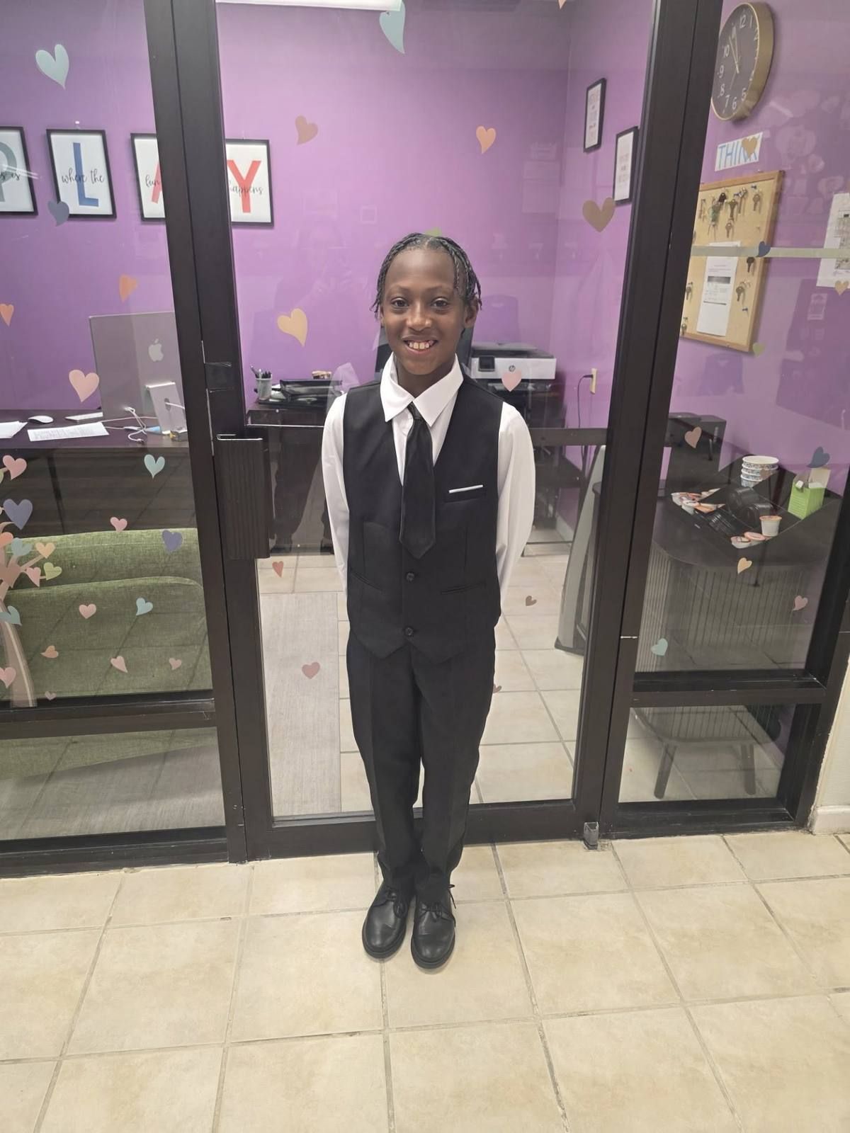 A school age boy dressed up in a vest and tie in the front office